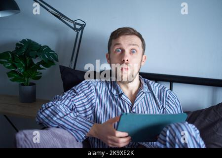 Young attractive man using tablet computer in bed in the morning. Young caucasian man using tablet device for shopping or education sitting on bed at bedroom. High quality image Stock Photo