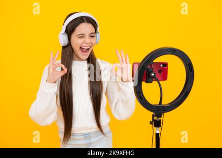 Blogging, videoblog. Teenager child blogger with phone recording video on isolated yellow studio background. Influencer teen girl speaking in front of Stock Photo