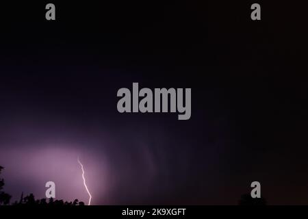 Lightning discharges in the stormy sky under dark rain clouds at night Stock Photo