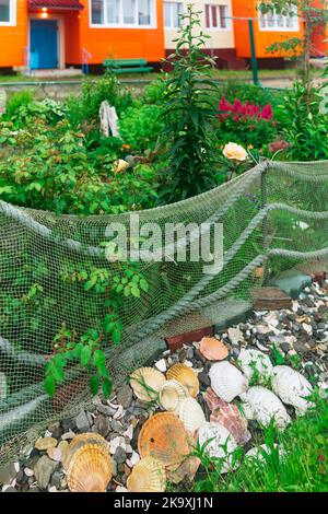 landscape design in a seaside village, a flower bed fence made from an old fishing net and a decorative border made of sea shells Stock Photo