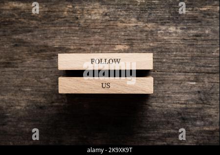 Follow us sign written on two wooden pegs placed over rustic wooden background. Stock Photo