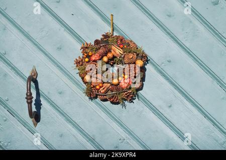 Blue wooden door with wrought iron handle and a wreath of dried plants in autumn. Stock Photo