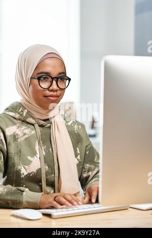 Young modern IT support manager or programmer sitting in front of computer monitor by workplace and developing new program Stock Photo