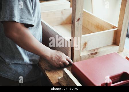 A carpenter measures the planks to assemble the parts, and build a wooden table for the customer. Stock Photo