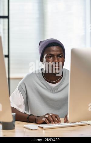 Young serious African American man in casualwear working over new software development in front of computer monitor in office Stock Photo