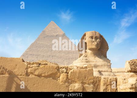 Egyptian Great Sphinx full body portrait with head, feet with all pyramids of Menkaure, Khafre, Khufu in background on a clear, blue sky day in Giza Stock Photo