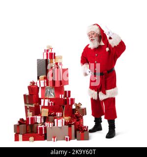 Santa Claus putting boxes into large pile of Christmas gifts isolated on white background Stock Photo