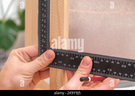 Carpenter using carpenter square to mark the line of wood cut for construction with a pencil. A close-up of the Master Carpenter's hands marks with pencil and carpenter square on a wooden board. DIY Stock Photo