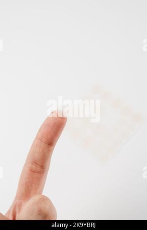 Close-up round acne patch on finger on white background. Acne patches for treatment of pimple and rosacea close-up. Facial rejuvenation cleansing cosm Stock Photo