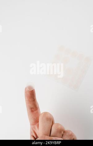 Close-up round acne patch on finger on white background. Acne patches for treatment of pimple and rosacea close-up. Facial rejuvenation cleansing cosm Stock Photo