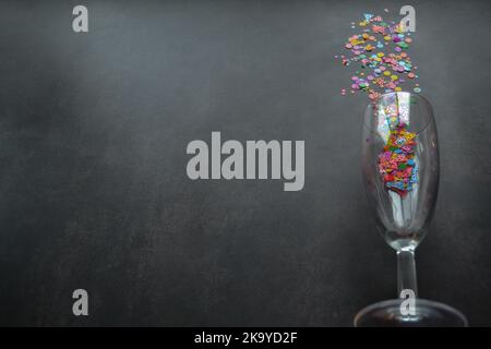 A wine glass with splashes of confetti on dark background. Copy space. Concept of party, celebration, New year, Christmas, birthday Stock Photo