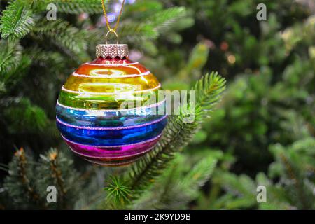 Bright glass rainbow colored Christmas ball, bauble hanging on a green artificial christmas tree. The concept of holiday, Christmas, symbol of the rai Stock Photo