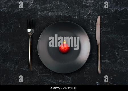 Christmas table setting with red Christmas ball on empty black plate and cutlery on black background. Top view, flat lay. Stock Photo