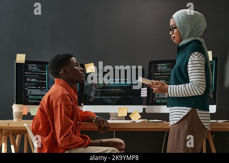 Two young confident multicultural interns in casualwear looking at each other during discussion of working points at meeting Stock Photo