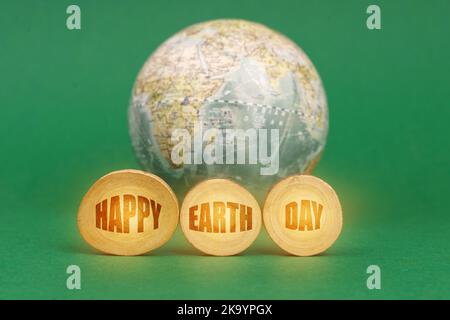 Ecological concept. On a green background, a globe and wooden circles with the inscription - Happy Earth Day Stock Photo