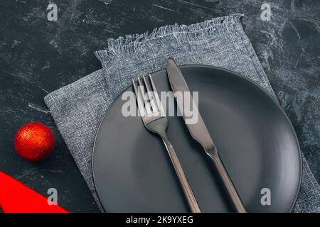 Christmas table setting with red Christmas ball, black plate and cutlery on black background. Top view. Stock Photo