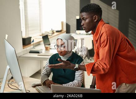 Young confident businessman consulting with Muslim female colleague during presentation of online information or project points Stock Photo