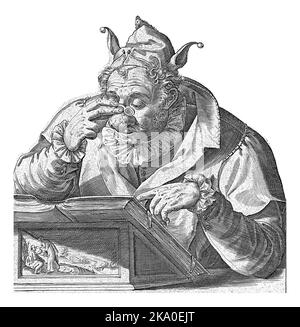 A man with a jester hood on his head and glasses on his swollen nose sits in front of a lectern on which lies a book - open, but with the cover up. Stock Photo