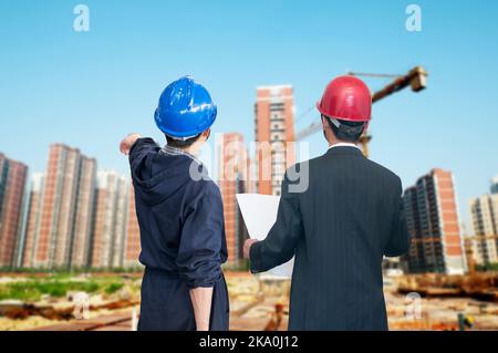 architects looking at blueprint in front of construction site Stock Photo