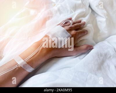 patient on hospital bed with blurry of Saline intravenous (iv) drip on hand in hospital, Needles and saline tubes are punctured on the patient's hand, Stock Photo