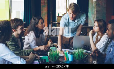 Multiracial group of professionals creative team is discussing charts and graphs developing working strategy at desk in shared office. Discussion, teamwork and workplace concept. Stock Photo