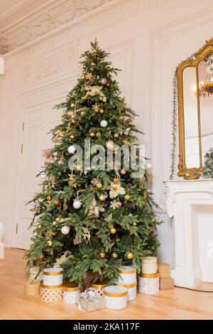 luxury gift boxes under Christmas tree, New Year home decorations, wrapping golden presents from Santa , festive tree decorated with garland,toys and Stock Photo