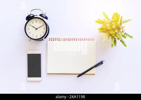 Flat lay top view of white table with notebook, a pen, smartphone and green plant Stock Photo
