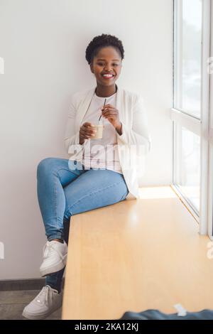 Photo of positive dark skinned woman enjoying good rest at coffee shop, drinking ice beverage. Drinking cocktails and having fun. Carefree african Stock Photo