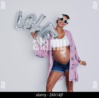 All she feels is love and joy. Studio shot of a beautiful young pregnant woman holding up a word balloon that reads love against a gray background. Stock Photo