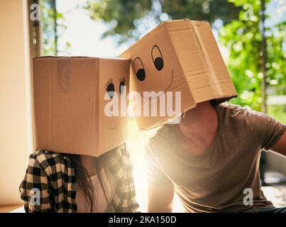 The big move has put the biggest smiles on their faces. a couple wearing boxes with smiley faces drawn on them on their heads. Stock Photo