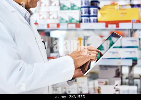 He sends his patients a monthly digital newsletter. Closeup shot of an unrecognizable pharmacist using a digital tablet in a chemist. Stock Photo