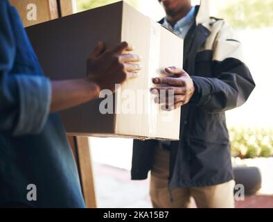 It has arrived. an unrecognizable woman receiving a package from a deliveryman at home during the day. Stock Photo