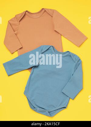 Two multi-colored children's bodysuits with long sleeves on a yellow background, top view Stock Photo