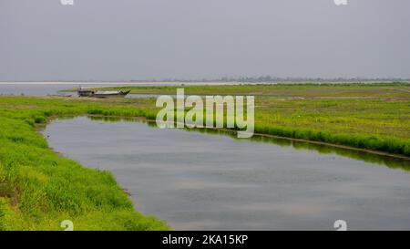 Scenic landscape view of marshlands along Brahmaputra river bank with wooden boat near Dibrugarh, Assam, India Stock Photo