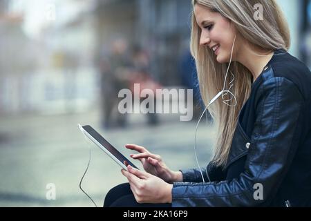 When the movies that good youve gotta watch it now. an attractive woman using a digital tablet and earphones in the city. Stock Photo