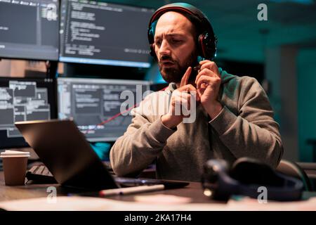 Software developer writing source code to create new user interface, programming html script and testing headset microphone. Working on developing system with multiple screens at night. Stock Photo