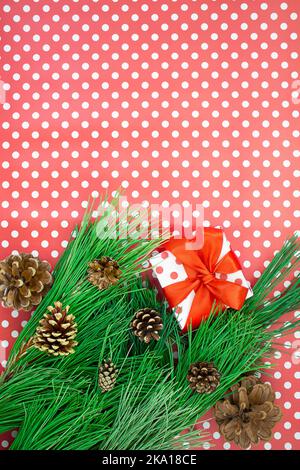Fir branches with cones, gift box with bow on red background with polka dots. Christmas, new year. Copy space Stock Photo