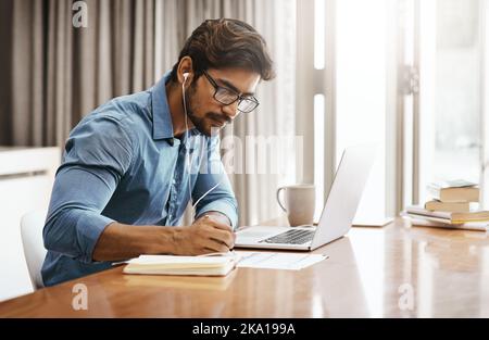 Writing down things that are important. a handsome young businessman working on his laptop in the office at home. Stock Photo