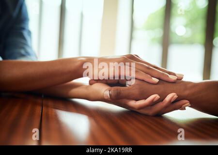 Just relax and everything will be fine. Closeup of two unrecognizable peoples hands holding each other while resting on top of a wooden table. Stock Photo