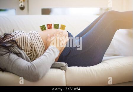 Taking time off to enjoy the last stretch of pregnancy. an unrecognizable young pregnant woman balancing wooden blocks on her tummy while relaxing on Stock Photo