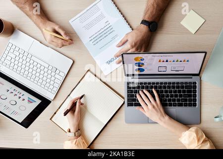 Hands of two young analysts or brokers using laptops and making notes while taking new online course of study for economists Stock Photo