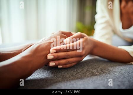 You have a friend in me. Closeup of two unrecognizable peoples hands holding each other while resting on top of a table. Stock Photo