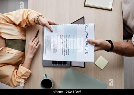 Above angle of young woman taking recommendation documents held by male applicant sitting in front and passing papers to her Stock Photo