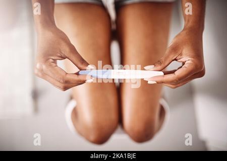 The best gifts in life are always unexpected. High angle shot of an unrecognizable woman taking a pregnancy test while sitting on the toilet. Stock Photo