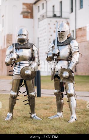 two knights in ancient metal armor stand at the stone wall of the castle Stock Photo