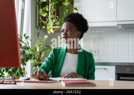 Concentrated on task African businesswoman working remotely on desktop computer in kitchen at home Stock Photo