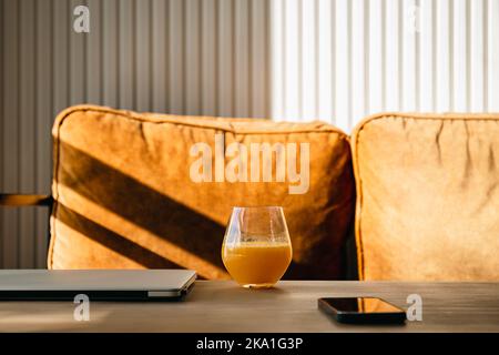 A glass of orange juice on the desktop near the laptop in the morning. Stock Photo