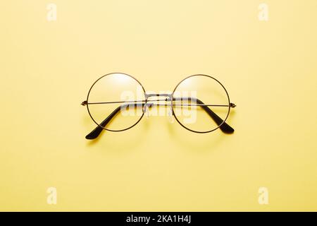 Glasses in round thin metal frame isolated on yellow surface. Stock Photo