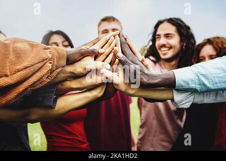 Group of multi-ethnic community of happy people having fun joining hands in the park - Multiethnic diverse group of college students high five - trust Stock Photo