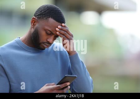 Concerned black man reading bad news on smart phone in the street Stock Photo